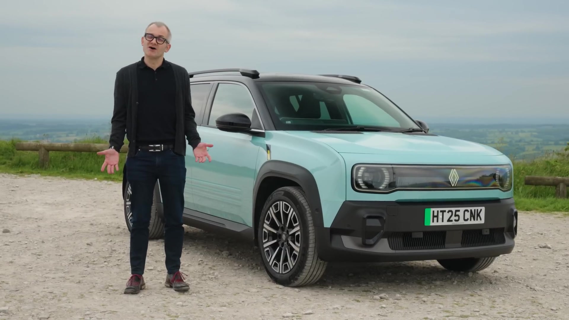 Lichtblauwe elektrische Renault 4 E-Tech van voren op een parkeerplaats in de heuvels, met een tester ernaast
